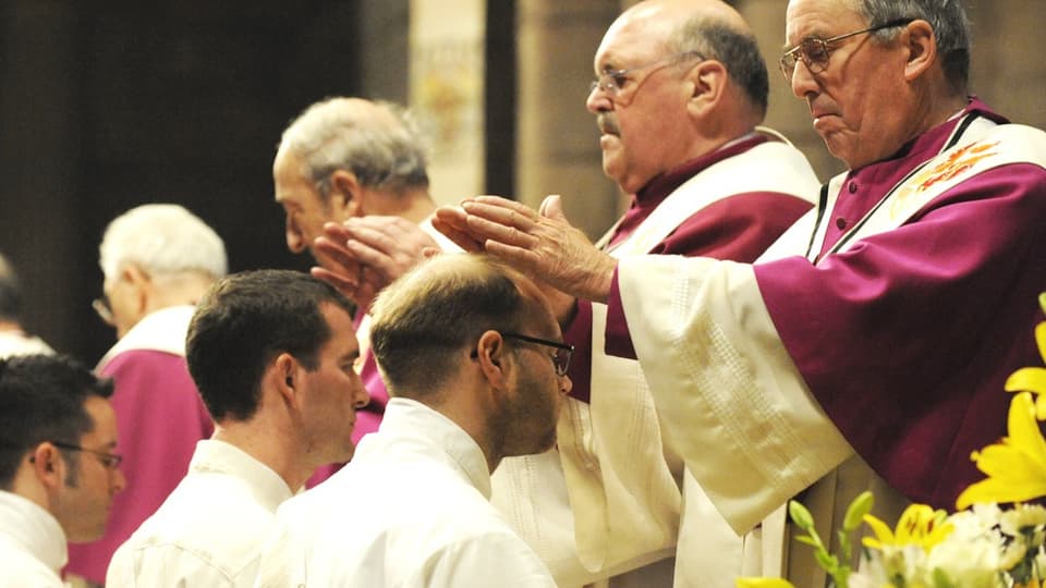 Priester in Ordensgewändern legen Novizen bei deren Priesterweihe die Hand auf