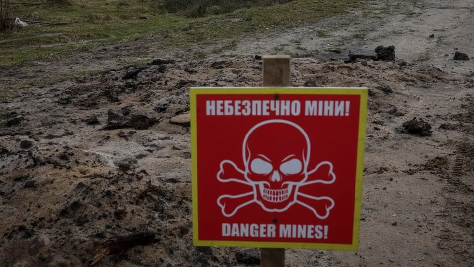 Ein Schild warnt vor der Gefahr von Minen auf einem Feld.