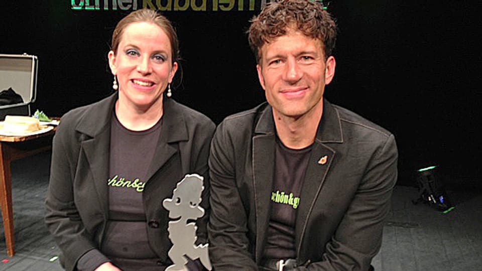 Das Kabarett-Duo schwarz gekleidet mit dem Cornichon-Preis aus Metall. 