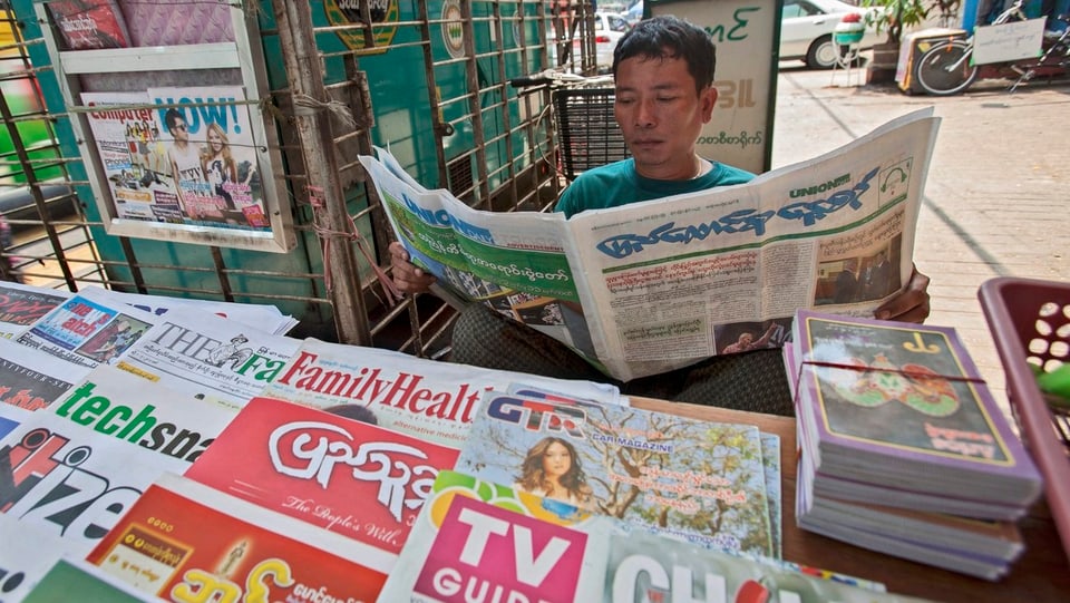 Mann mit burmesischer Zeitung in der Hand an einem Kiosk.