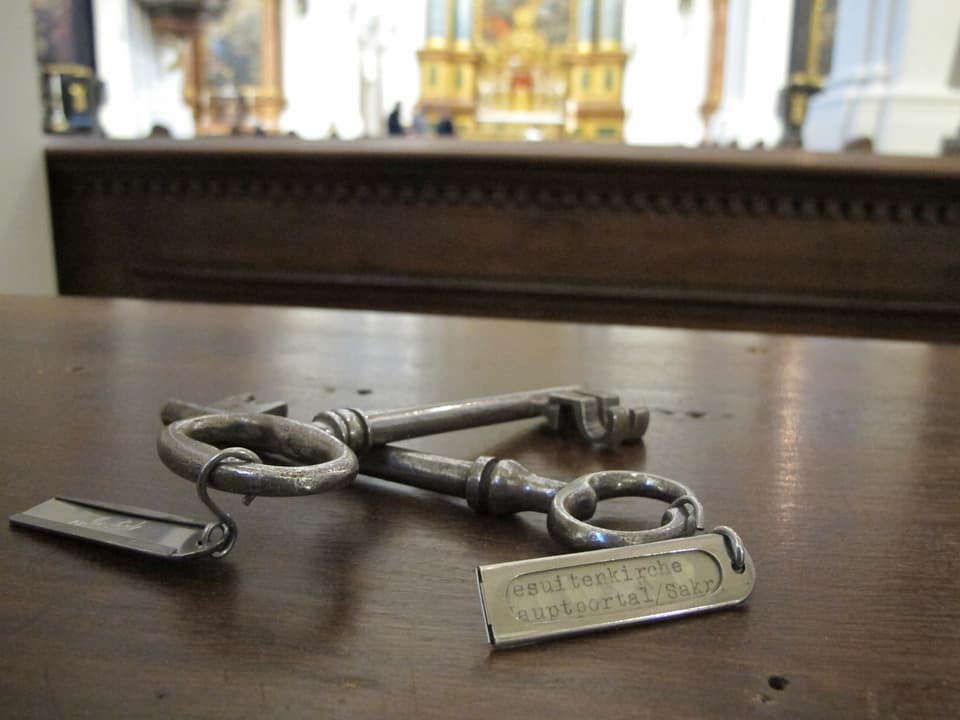 Zwei grosse Metall-Schlüssel - mit Schildchen - liegen auf einer Holzablage.