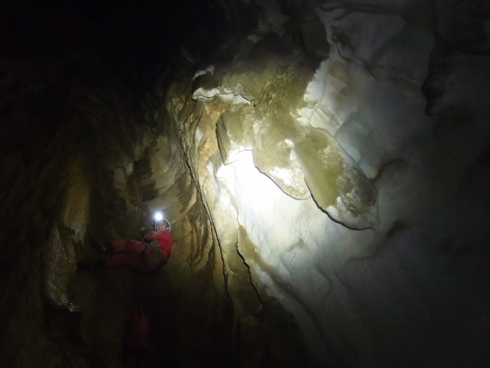 In einer dunklen Schachthöhle ist Sarah Allemann im Stirnlampen-Licht knapp sichtbar.
