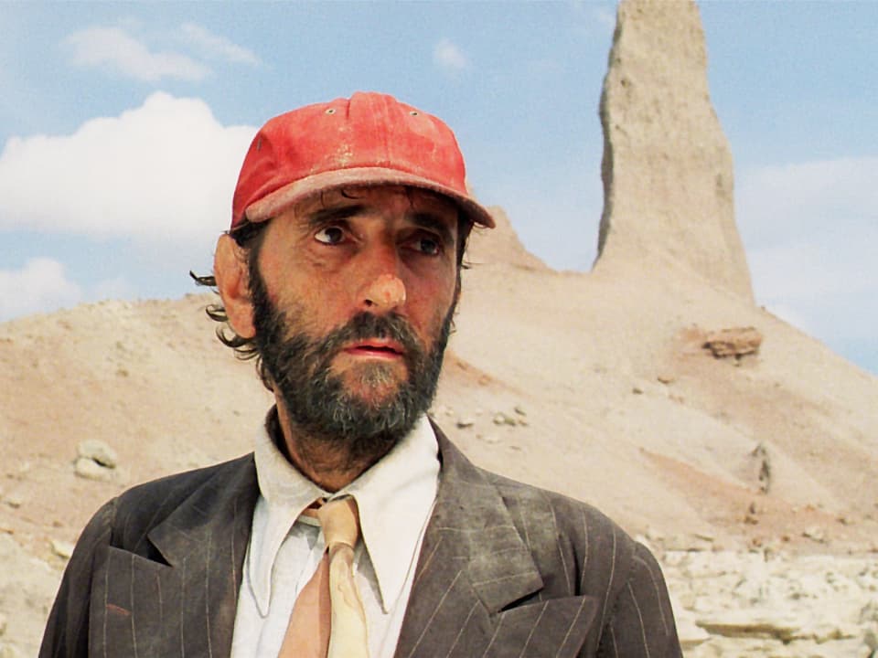 Mann mit roter Kappe in der Wüste.