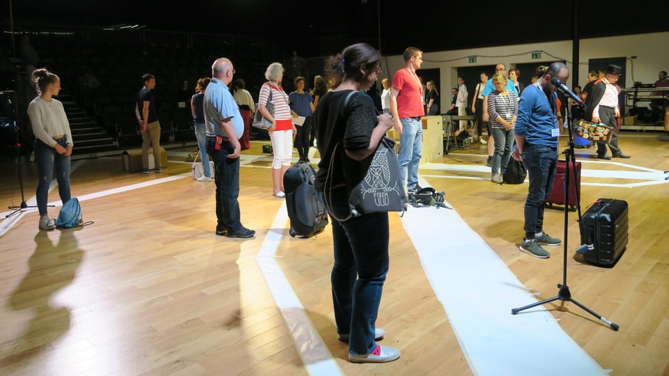 Mit gepackten Koffern stehen mehrere Laienschauspieler auf einer Bühne.