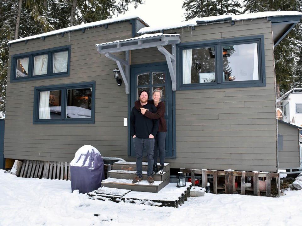 Mann und Frau vor dunklem Haus auf Rädern in weissem Schnee. 