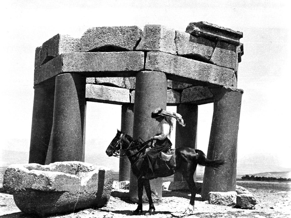 Frau sitzt auf Pferd vor einem Monument auf Stein.