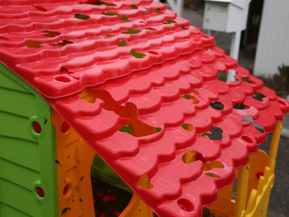Rotes Plastikdach eines Spielhauses für Kinder. Darin viele Löcher vom Hagelschlag. 