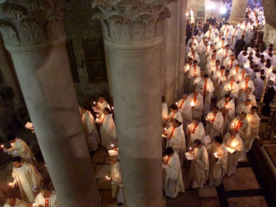 In einer Kirche laufen viele Personen mit weissen Gewändern und Kerzen in der Hand in einer Prozession