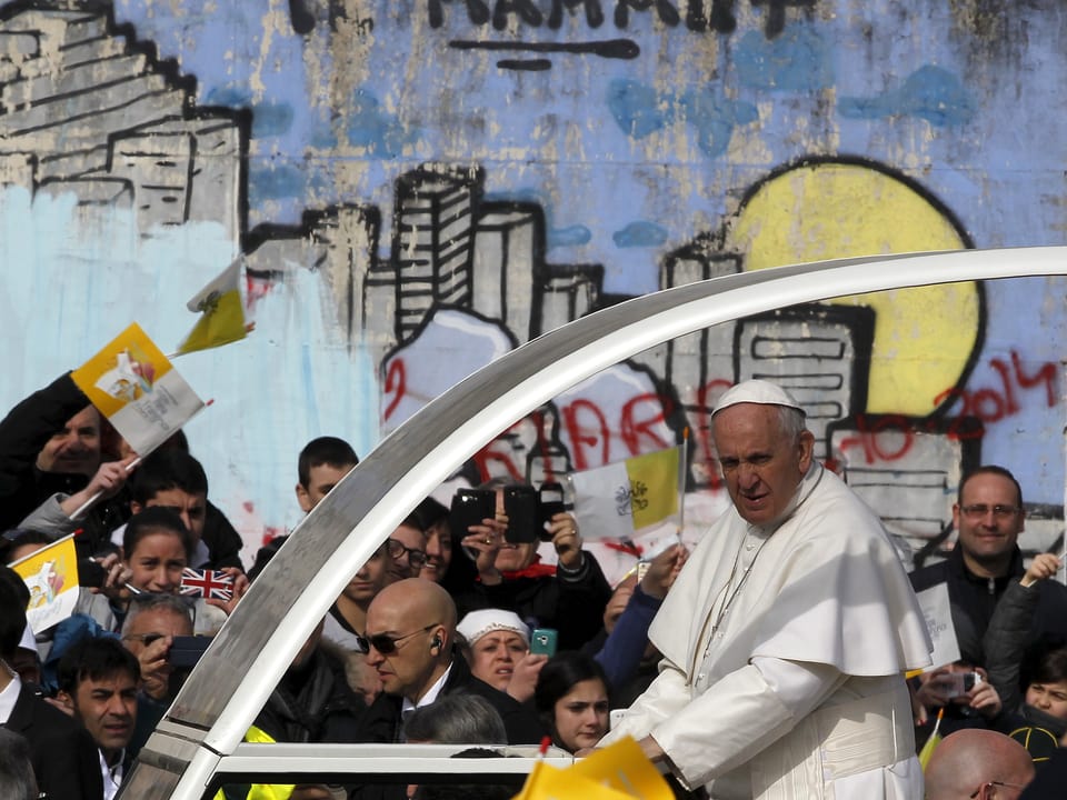 Franziskus im Papamobil vor einem Graffitti.