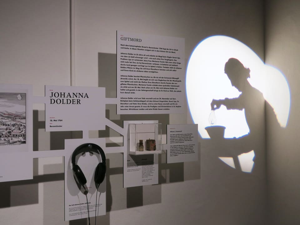 Texttafeln einer Ausstellung, dazu ein Kopfhörer und die Umrisse einer Frauengestalt, die auf eine Wand projiziert wird.