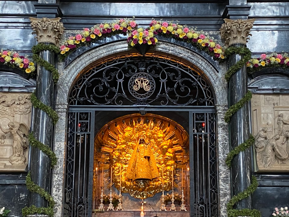 Eine schwarze Madonna-Figur, in goldene Kleider gehüllt und von Goldornamenten umgeben.