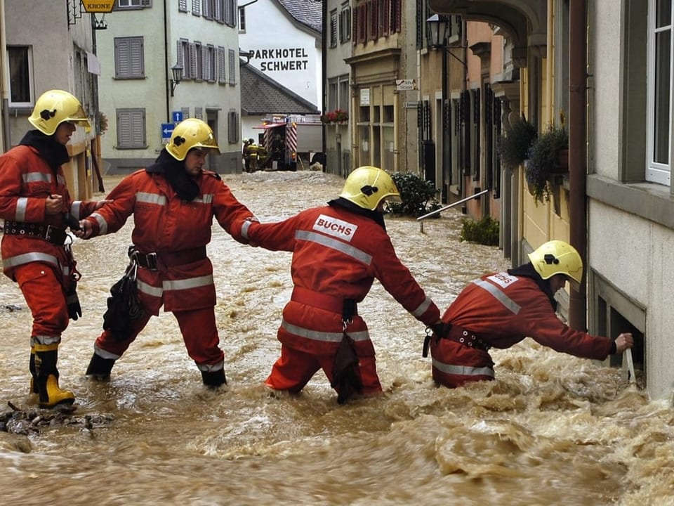 Vier Feuerwehrmänner helfen sich gegenseitig, nicht in den Fluten zu versinken.