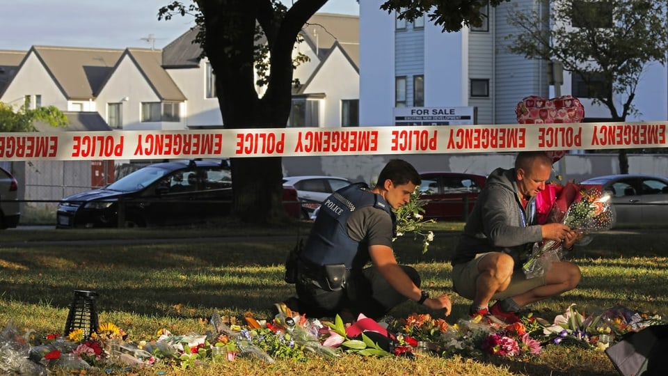 Zwei Polizisten heben Blumen hoch, die vor der Moschee in Christchurch niedergelegt wurden, nachdem dort das Attentat geschah.