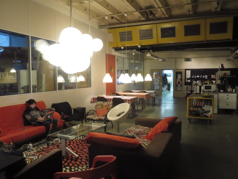 Ein grosser Raum mit Sofas und Tischen. Eine Frau sitzt an einem Laptop.