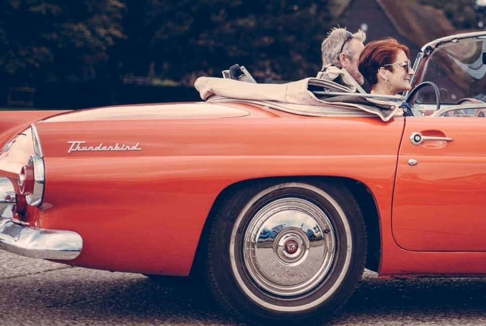 Ein Mann und ein Frau sitzen in einem alten roten Auto.