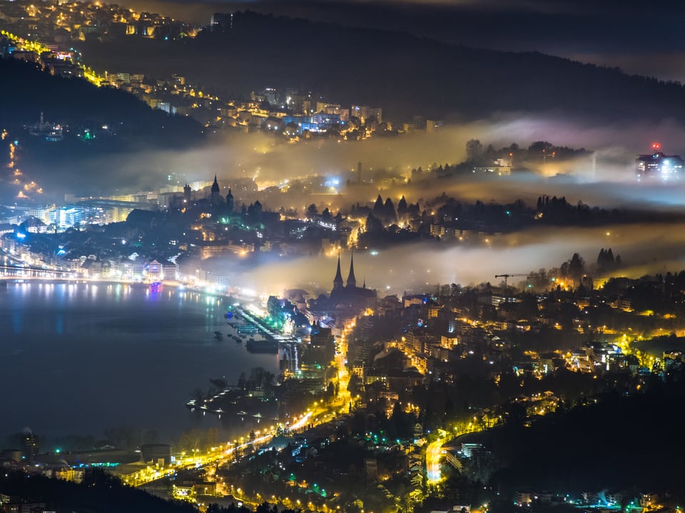 Ein Lichtermeer rund um das Luzerner Hafenbecken ist zu sehen. Über der Stadt liegen zwei grosse Nebelschwaden.