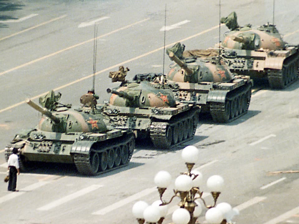 Ein Mann steht vor einer Kolonne von vier Militärpanzern in China.