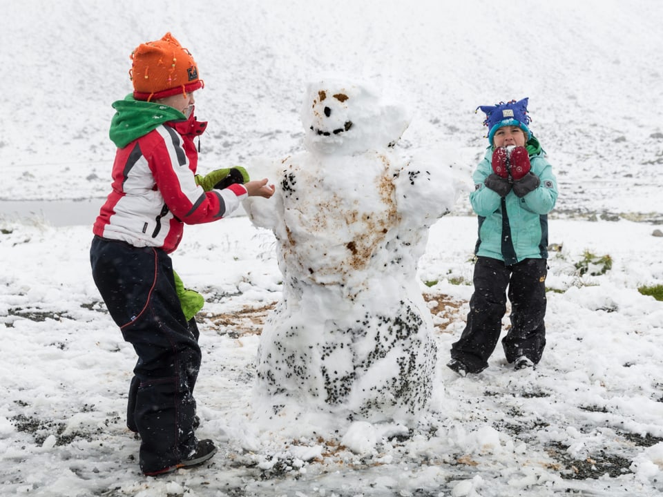 Zwei Mädchen in Skianzügen bauen einen Schneemann