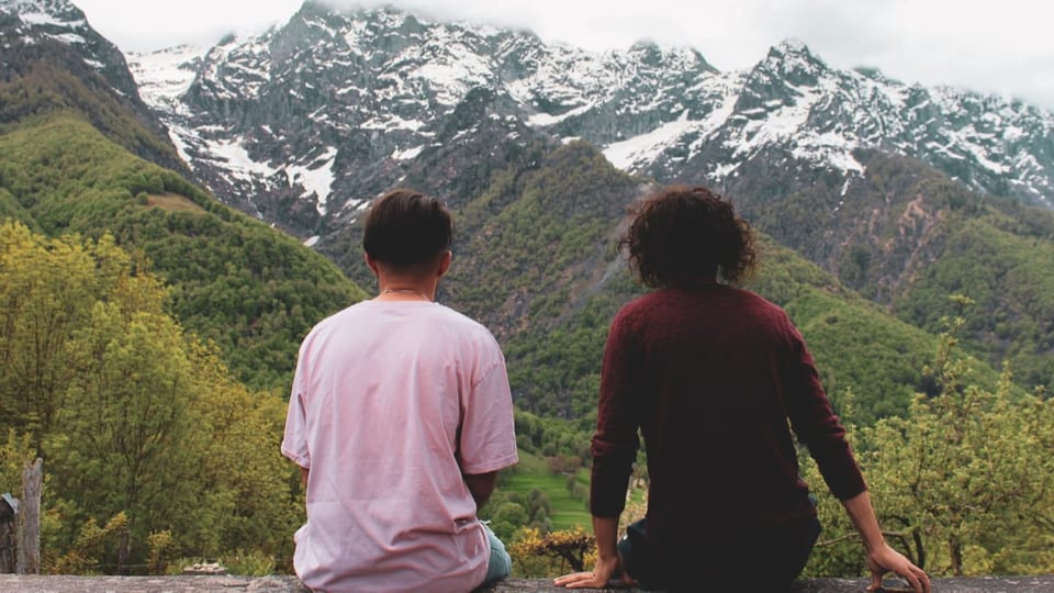 zwei junge Menschen sitzen auf einer Bank und schauen aufs Bergpanorama