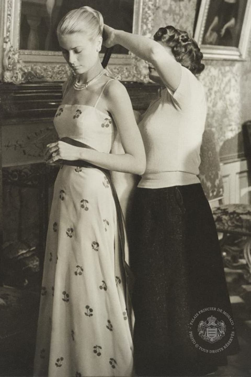 Eine Garderobiere flechtet Grace Kelly ein Haarband ins Haar. 