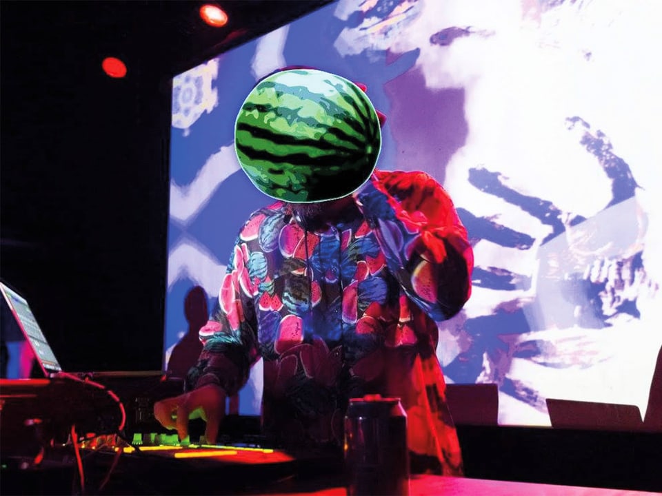 Ein DJ am DJ-Pult. Sein Kopf ist mit einer Wassermelone bedeckt.