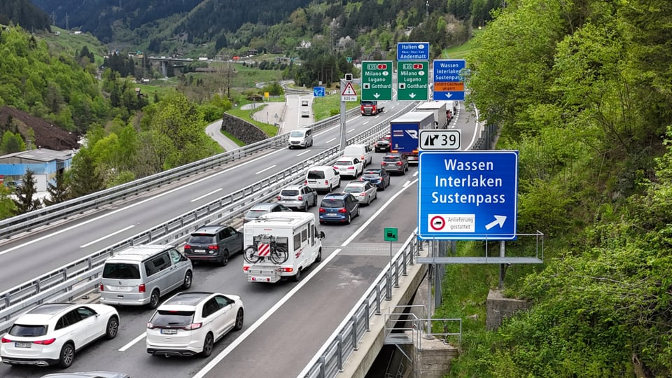Verkehrsstau auf einer mehrspurigen Autobahn in bergiger Landschaft mit Wegweisern