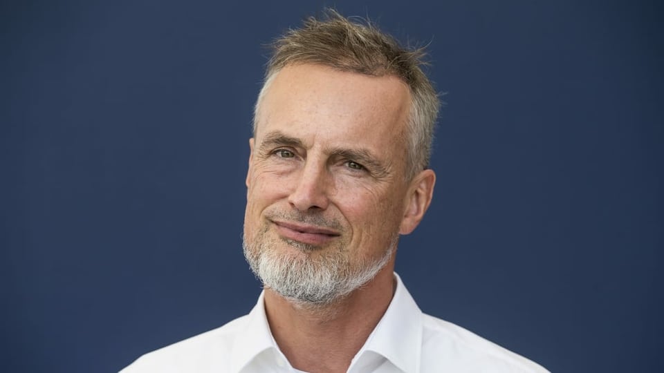 Jürgen Schmidhuber trägt ein weisses Hemd, einen Spitzbart und braunes, kurzes Haar.
