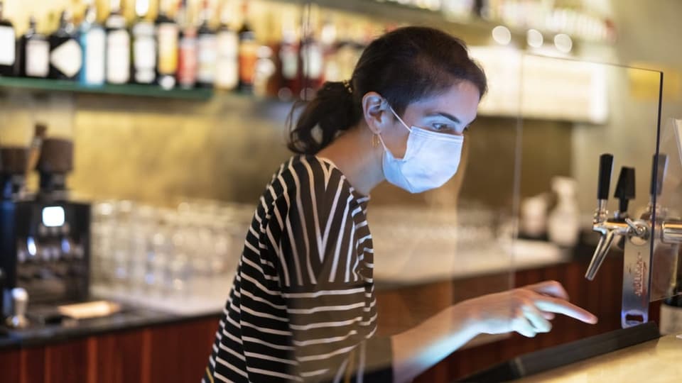 Eine junge Frau mit Gesichtsmaske bedient eine Kasse in einem Restaurant