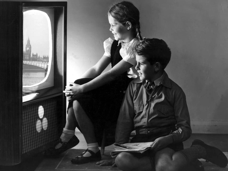 Schwarzweiss-Bild: Ein Junge und ein Mädchen sitzen vor einem Fernseher. 