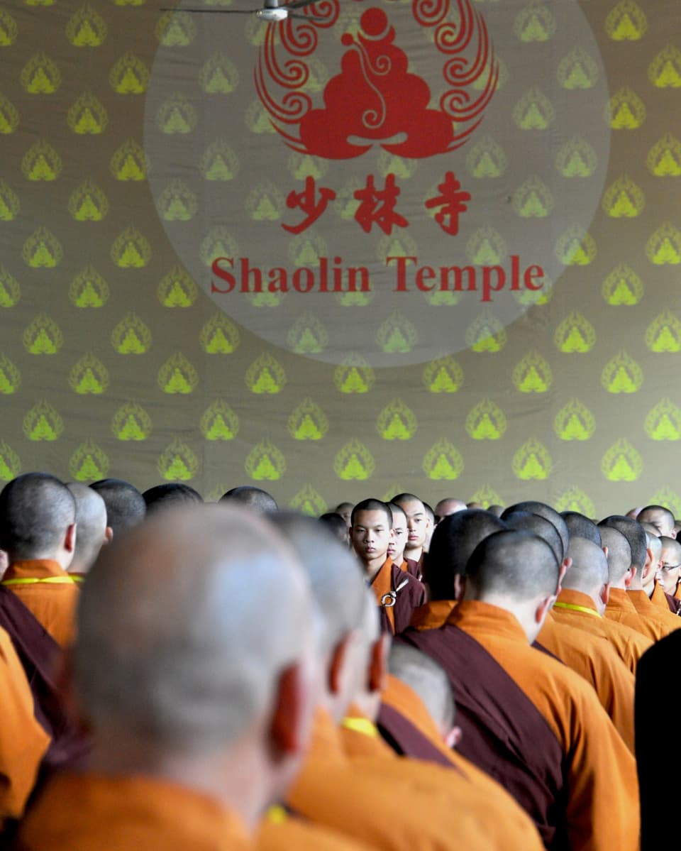 Sitzende Mönche vor einer Wand mit der Aufschrift "Shaolin Temple".
