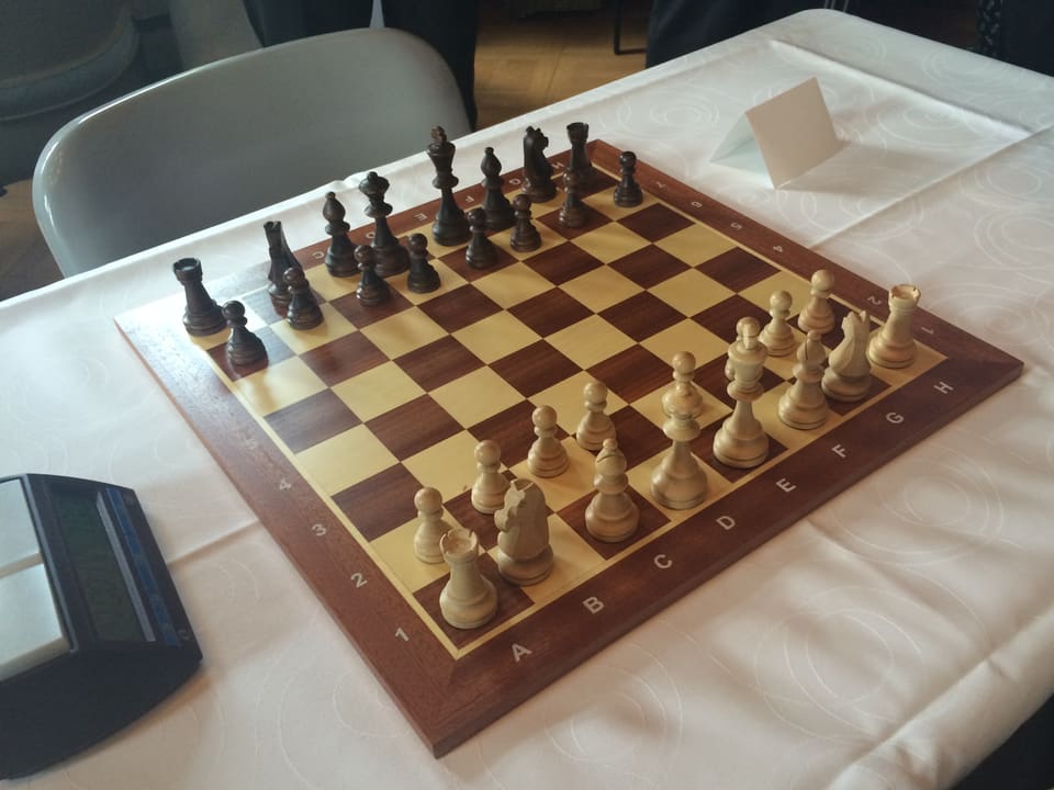 Schachbrett mit allen Figuren, bereit zum Spiel. Links eine Schachuhr mit zwei Tasten oben.