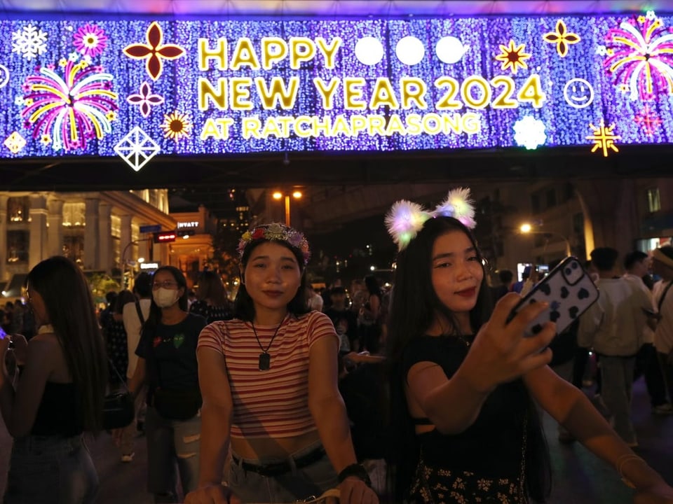 Zwei Frauen stehen vor einem Leuchtschild mit Neujahrwünschen und machen ein Selfie.