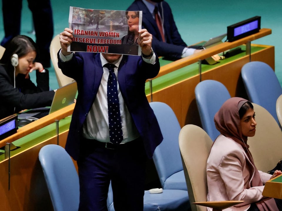 Der israelische Botschafter hebt ein Bild hoch auf in roten Buchstaben steht «Iranian women deserve freedom now!»