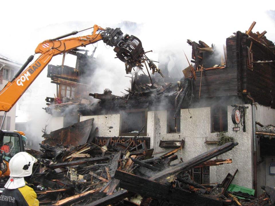 Ein Kran bricht Teile aus dem abgebrannten Gebäude heraus.