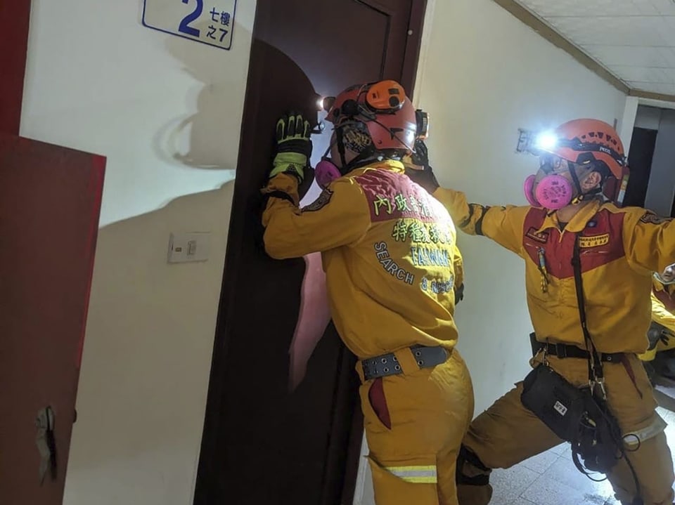 Rettungskräfte stehen in einem schiefen Gebäude und stehen an einer geschlossenen Türe.