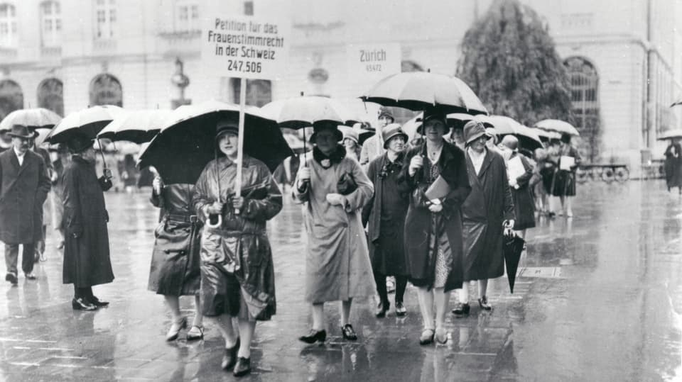 eine schwarz-weiss Fotografie von Frauen mit einem Plakat und Regenschirmen