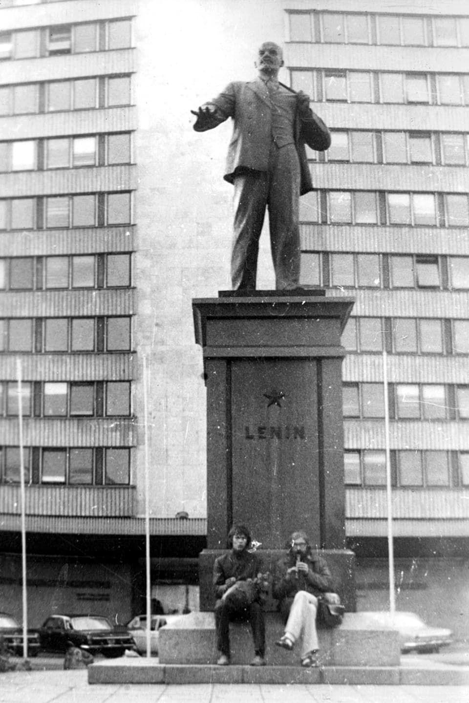 Altes Foto: Zwei Männer sitzen vor dem Sockel einer Lenin-Statue. Einer Spielt Blockflöte.