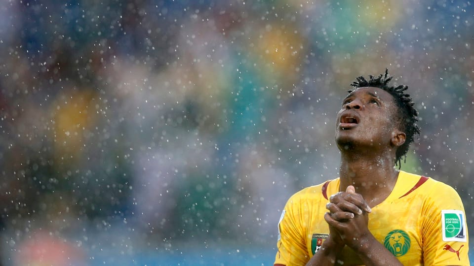 Brasilianischer Nationalfussballer betet mit Blick zum Himmel in strömendem Regen.