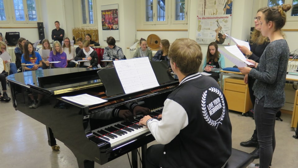 Ein Studierender spielt am Piano, Schüler singen dazu.