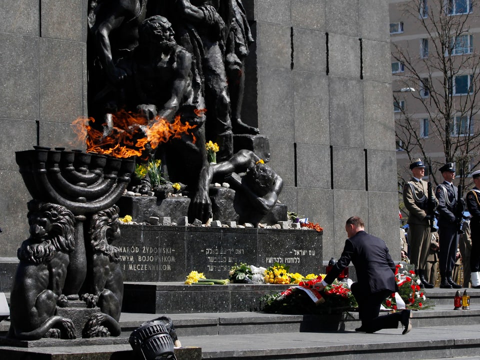 Eine Person kniet vor dem Sockel eines Denkmals.