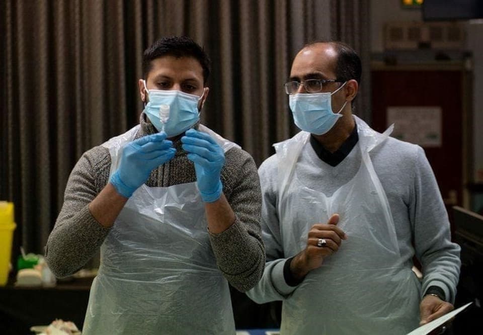 Zwei Männer in Schutzkleidung bereiten eine Covid-Impfung vor.