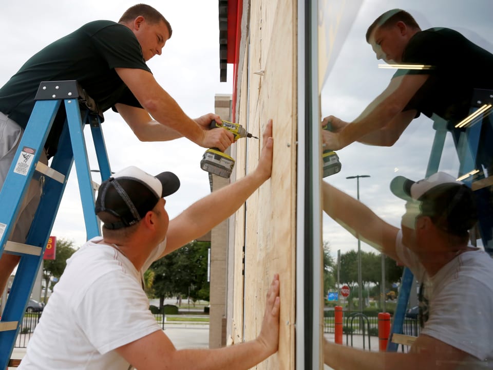 Zwei Männer montieren Holzplatten an ein Gebäude.