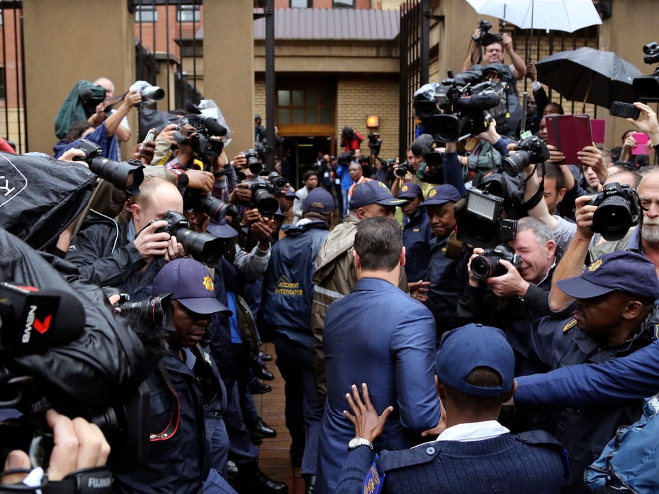 Medienandrang, in der Mitte geht ein Mann in blauem Anzug