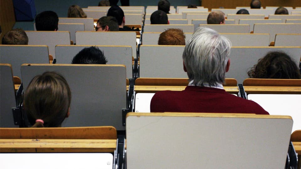 Blick in einen Hörsaal mit gemischtem Publikum jeden Alters.