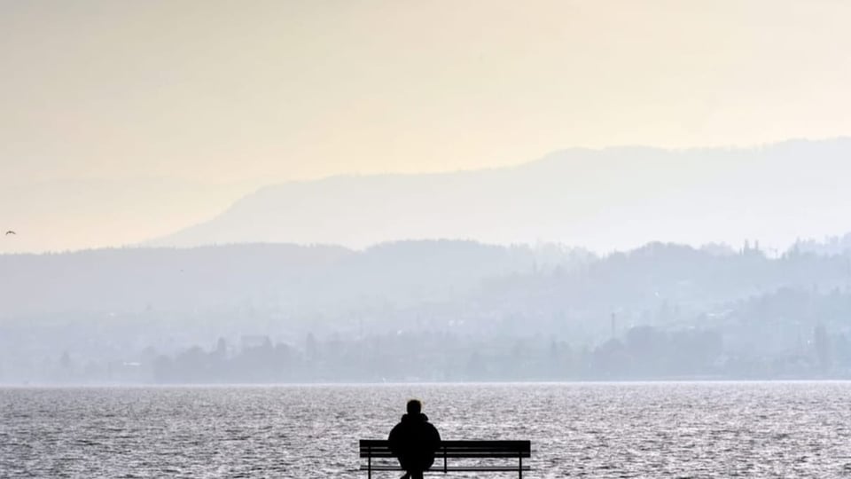 Ein Mann sitzt alleine auf einer Bank am Zürichsee.