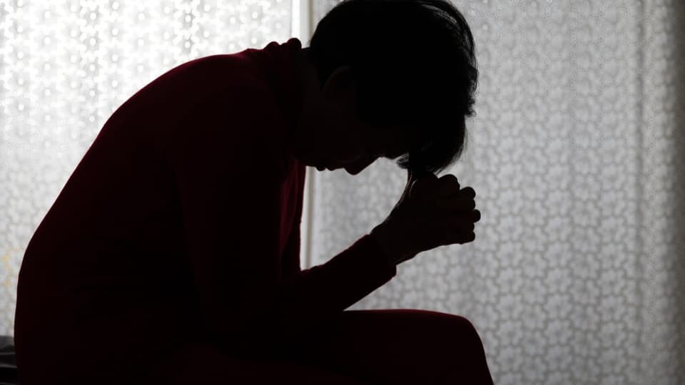Verzweifelte Frau im Schatten, stützt den Kopf auf ihre Hände.