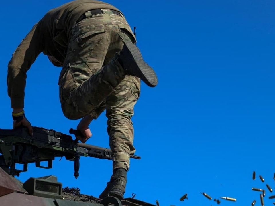 Man sieht den Rücken eines Mannes, der auf einem Panzer steht, daneben herunterfallende Patronenhülsen