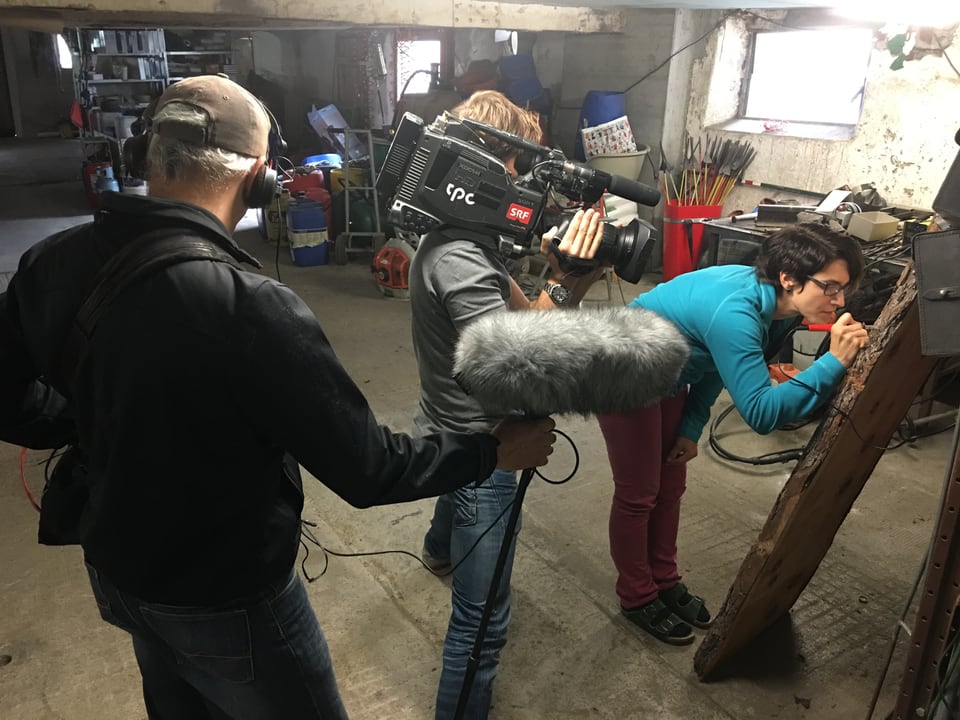 Nina und Kamerateam in der Werkstatt. Nina schnitzt ihr Menü in einen Baumstamm.