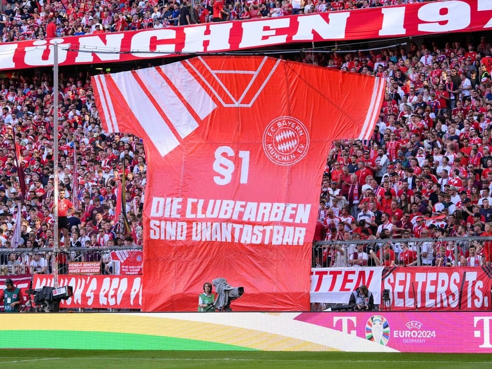 Grosses Banner von FC Bayern München im Fussballstadion mit Fans im Hintergrund.