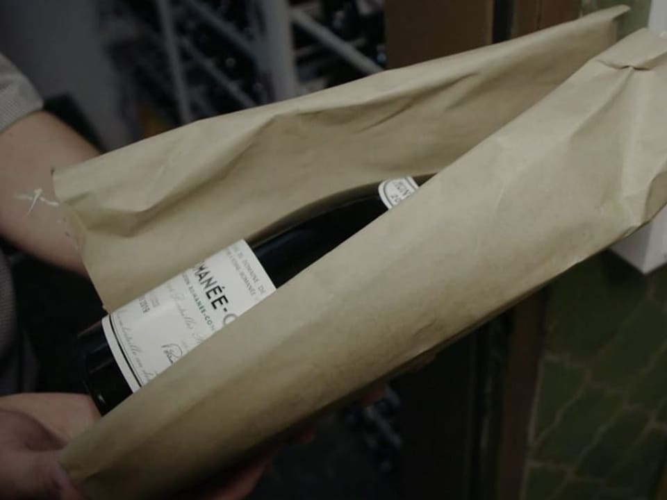 Weinflasche in braunem Papier verpackt, gehalten in einer Hand.